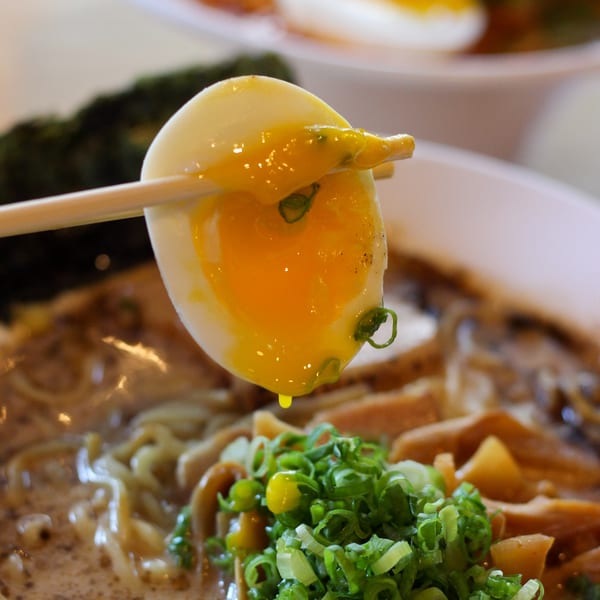 Chopsticks holding a soft-boiled egg with a runny yolk over a bowl of GoBistro ramen.