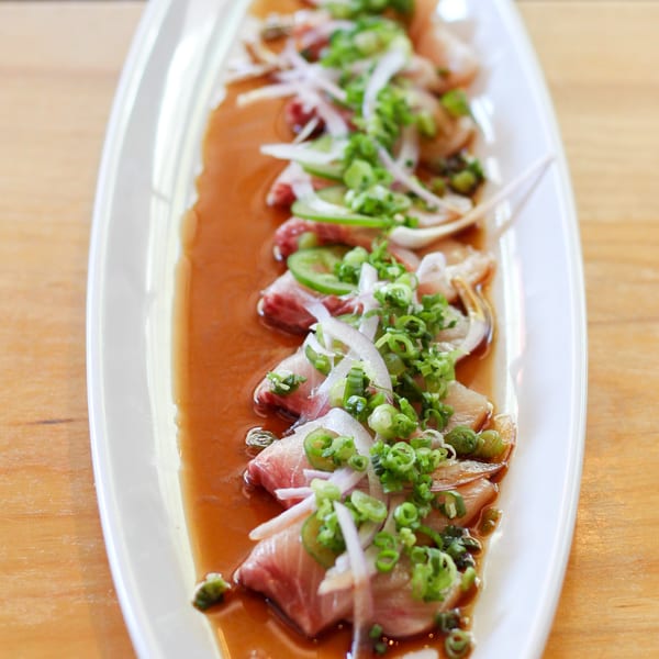 GoBistro's yellowtail sashimi with ponzu sauce, jalapeños, red onions, and scallions on a white plate.